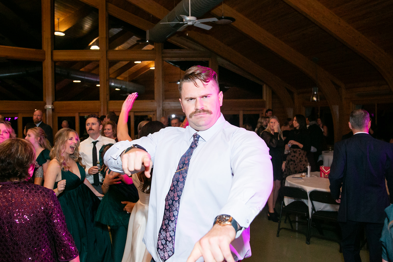 A wedding guest pointing at the camera while dancing under pink uplighting