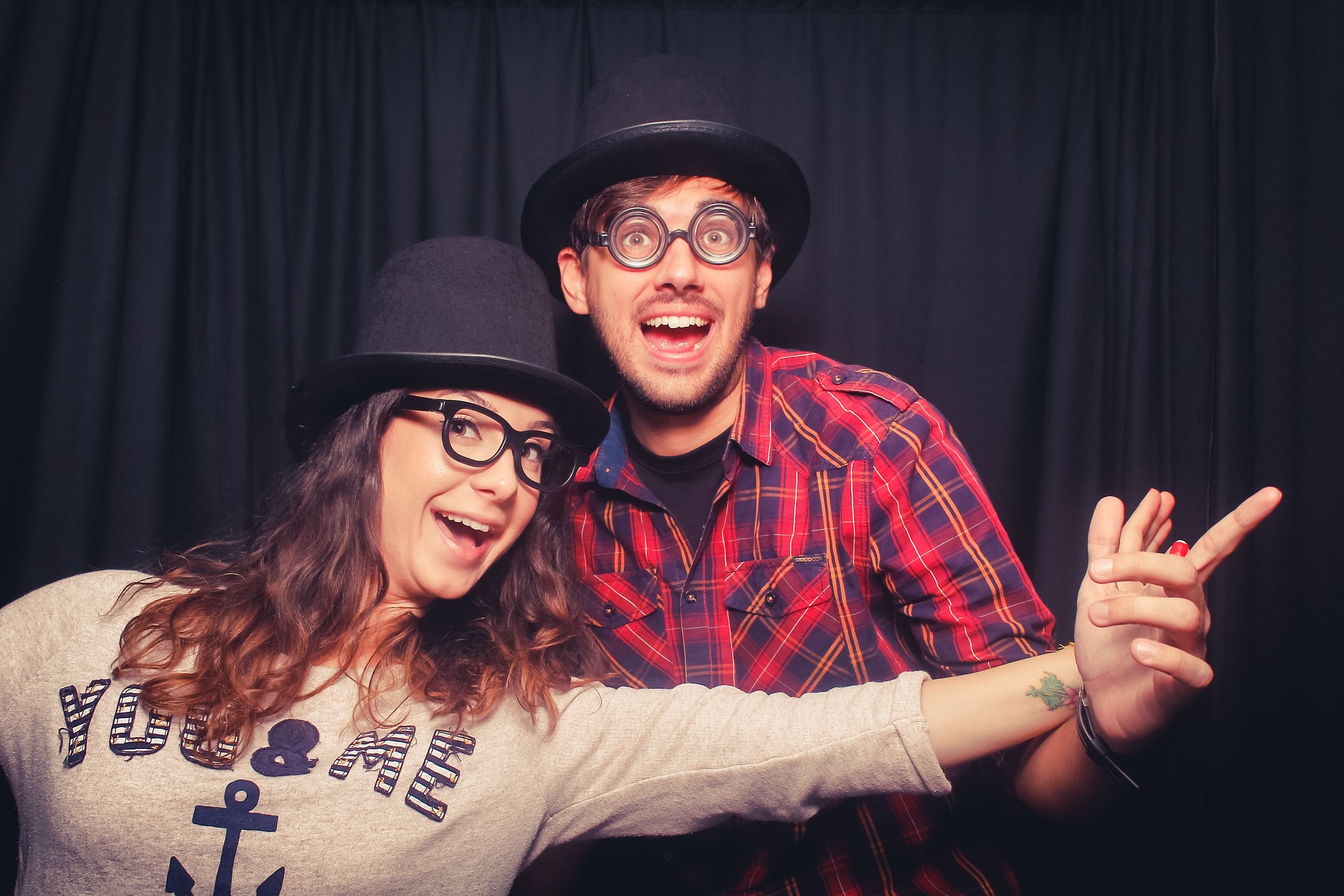 A couple in hats and playful glasses posing together in a photo booth